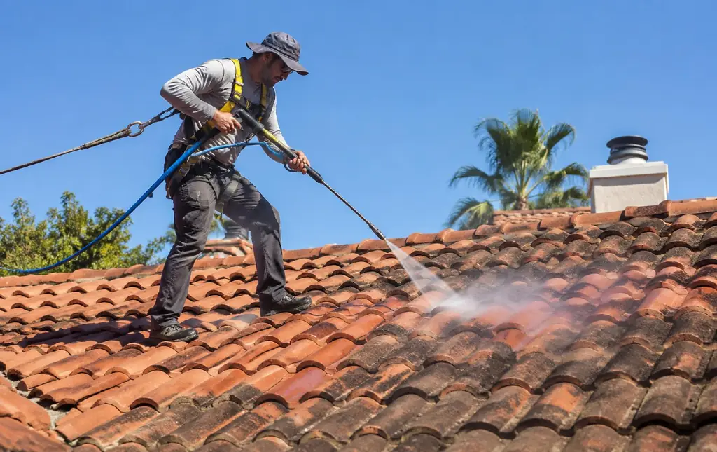 Technician in a safety harness soft washing a clay tile roof